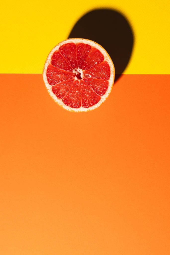 close up of half of red grapefruit and copy space on orange and yellow background. fruit, food, freshness and colour concept.